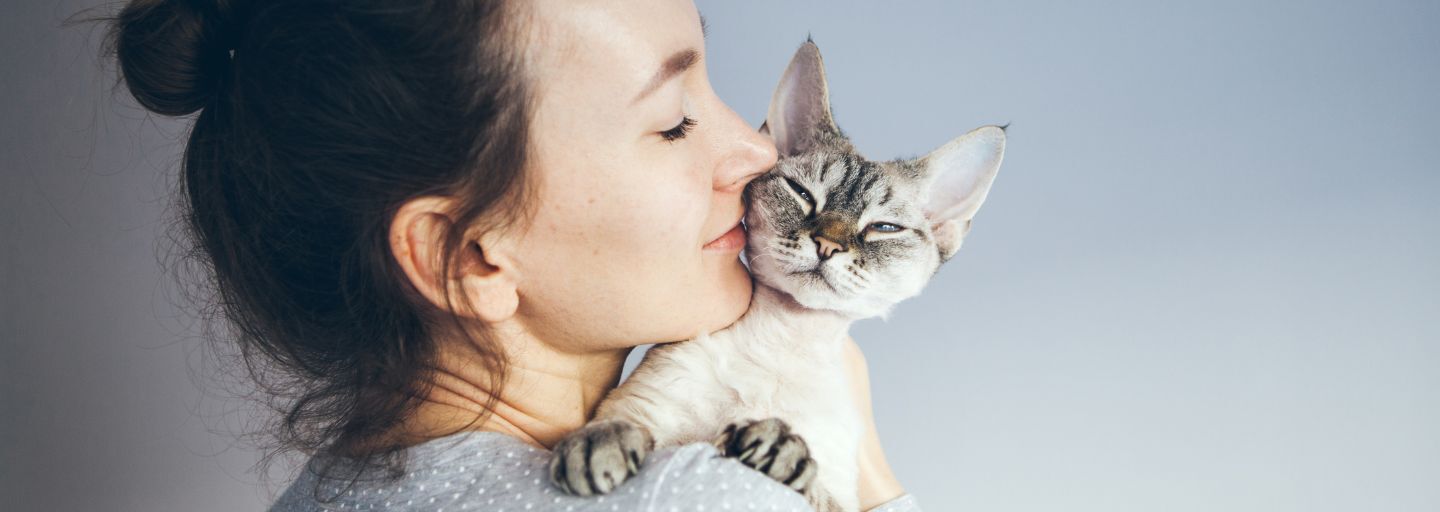 Casually dressed girl holding and kissing Devon Rex Cat.