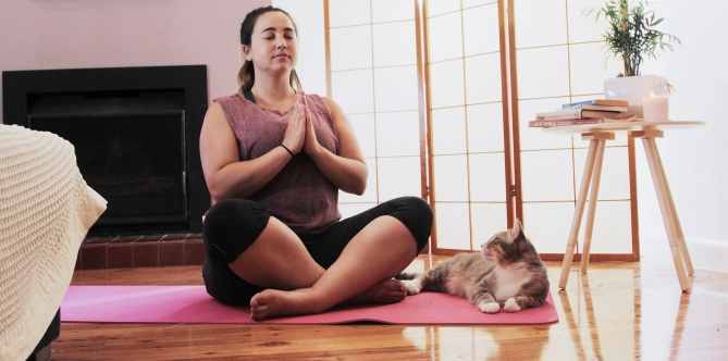 woman practicing yoga with cat laying next to her